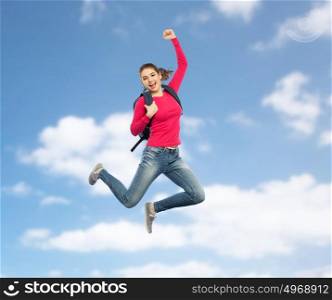 education, travel, tourism, motion and people concept - smiling young woman or student with backpack jumping in air over blue sky background. happy woman or student with backpack jumping