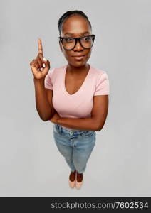 education, vision and people concept - african american woman in glasses with one finger up over grey background. african american woman in glasses with finger up