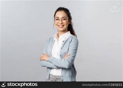 Education, women and lifestyle concept. Attractive asian female entrepreneur, girl tutor smiling satisfied, cross hands chest, pleased help customer with any question, grey background.. Education, women and lifestyle concept. Attractive asian female entrepreneur, girl tutor smiling satisfied, cross hands chest, pleased help customer with any question, grey background