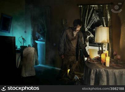 Eerie zombie man standing near dining table in living-room. Abandoned house interior with cobwebs. Eerie zombie man standing near dining table