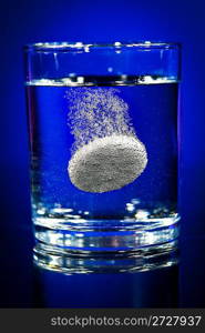 Effervescent tablet in water with bubbles on a blue background