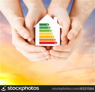 efficiency and home concept - close up of female hands holding paper house with energy saving rating over evening sky background. hands holding green paper house. hands holding green paper house