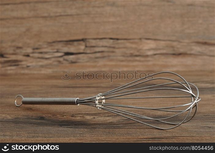 Egg beater, whisk, isolated on a wooden background