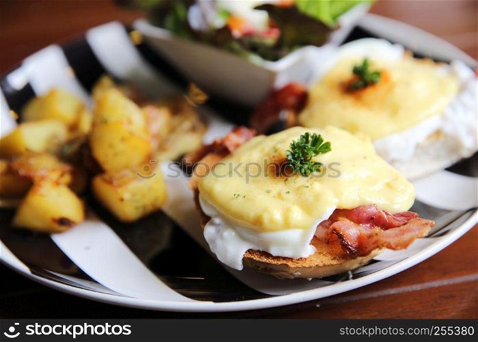 egg benedict with bacon and potato on wood background