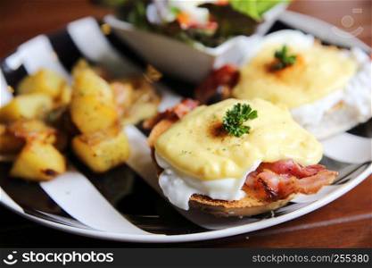 egg benedict with bacon and potato on wood background