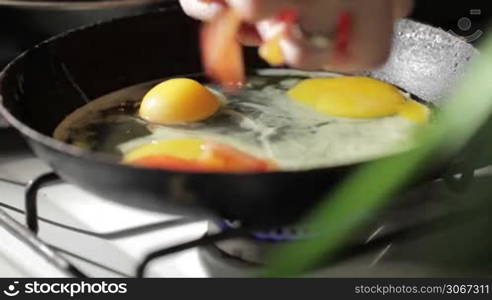 Egg frying in a pan. Adding tomato slices.