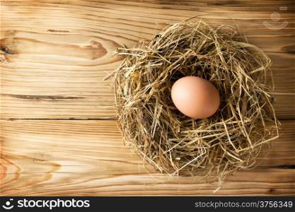 Egg in hay nest on wooden table background. Top view