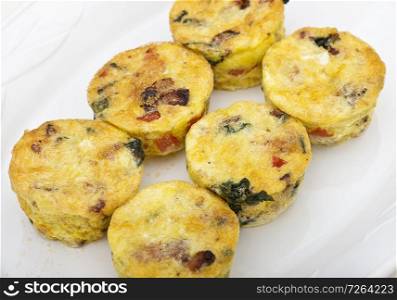 Egg muffins with spinach, bacon, cheese and tomatoes on white plate