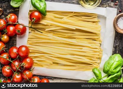 Egg Noodles in wrapping paper and fresh cooking ingredients: basil and tomatoes, top view close up