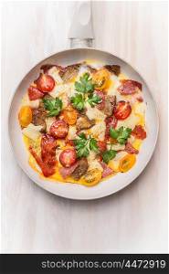 Egg omelette in white frypan with tomatoes,bread, cheese and sausage on white wooden background, top view, close up