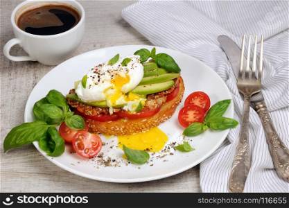 Egg poached on a toasted slice of baguette with tomato, spicy ham and avocado, sprinkled spices and basil