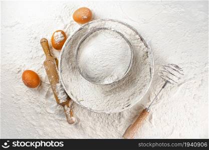 Egg, sieve and rolling pin on flour. Top view. On a white background. . Egg, sieve and rolling pin on flour. Top view.