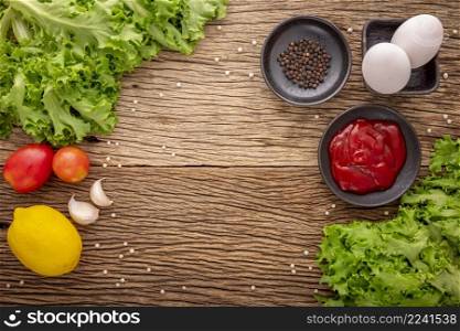 egg with ketchup, pepper, lettuce, tomato, garlic and lemon on rustic natural wood texture background, ingredient for prepare food, top view
