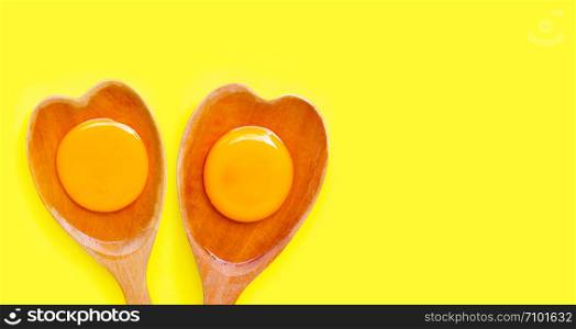 Egg yolk and white on wooden spoon heart shape on yellow background. Top view