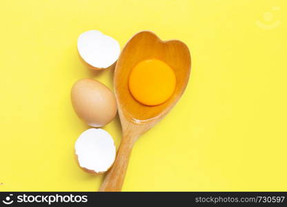 Egg yolk and white on wooden spoon heart shape on yellow background. . Top view