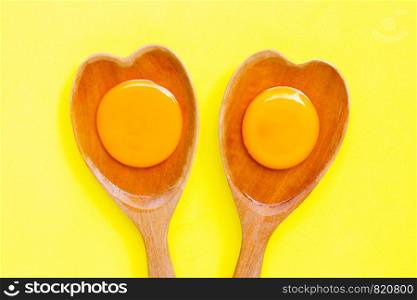 Egg yolk and white on wooden spoon heart shape on yellow background. Top view