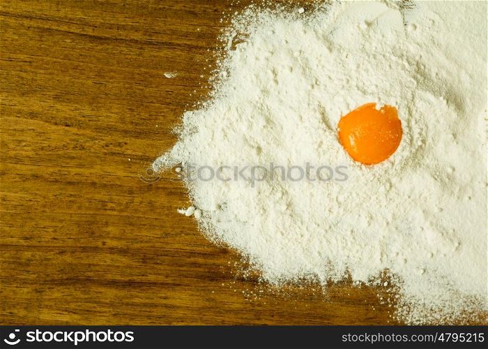 Egg yolk on a pile of flour on a wooden table
