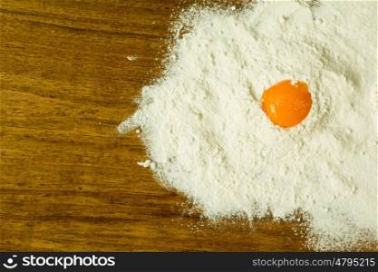 Egg yolk on a pile of flour on a wooden table