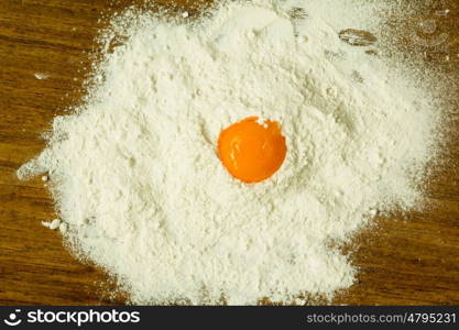 Egg yolk on a pile of flour on a wooden table