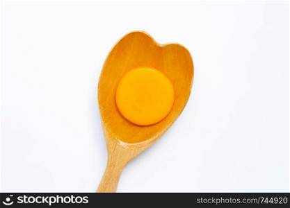 Egg yolk on wooden spoon on white background.