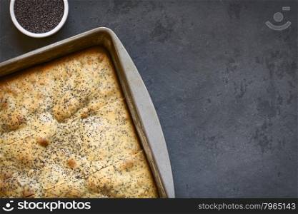 Eggnog and poppy seed cake in baking pan. Poppy seeds on the side, photographed overhead on slate with natural light.