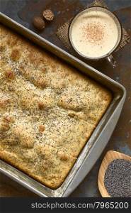 Eggnog and poppy seed cake in baking pan. Poppy seeds, eggnog and nutmeg on the side, photographed overhead on slate with natural light.