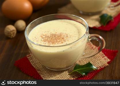 Eggnog drink in glass cup sprinkled with ground nutmeg, photographed on dark wood with natural light (Selective Focus, Focus one third into the eggnog and on the handle of the cup)