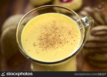 Eggnog with freshly grated nutmeg on the top, gingerbread and thumbprint cookies on the side, photographed with natural light (Selective Focus, Focus one third onto the top of the eggnog)