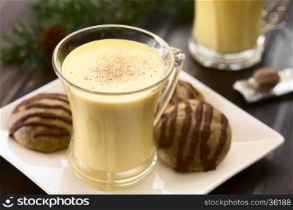 Eggnog with freshly grated nutmeg on the top, gingerbread cookies on the side, photographed with natural light (Selective Focus, Focus one third onto the top of the eggnog)