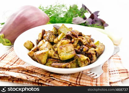 Eggplant fried with onions, eggs and spices in a plate on a towel, basil, leek and dill on a wooden board background