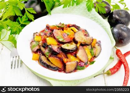 Eggplant fried with plums, onions and sweet peppers in a plate on a towel against light wooden board