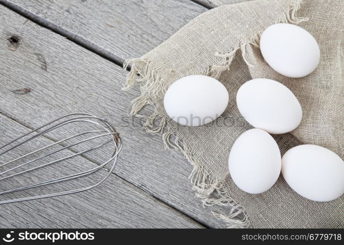 Eggs and whisk styled on a raw, aged wood background.