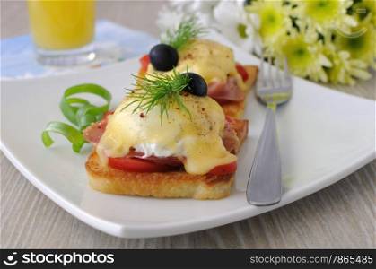 Eggs Benedict with ham and tomato on toast with cheese and orange juice