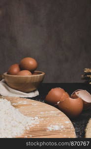 Eggs, dough, flour and rolling-pin on wooden table background. Preparation for making homemade ravioli pasta