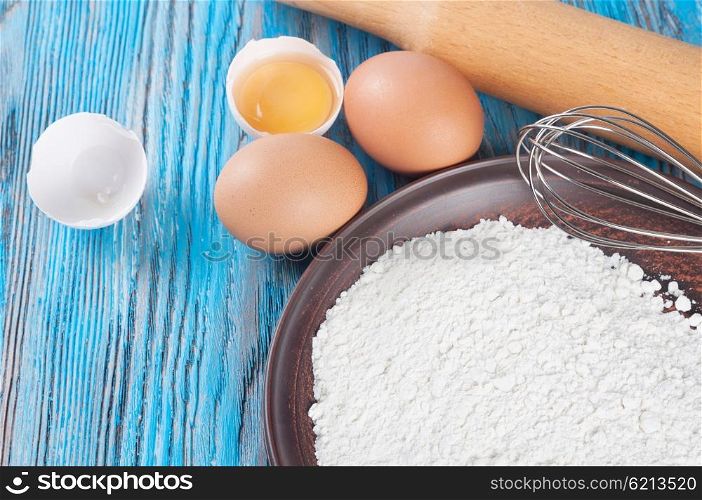 Eggs, egg yolk and flour on a blue wooden background