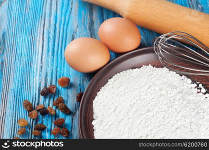 Eggs, flour and raisins on a blue wooden background
