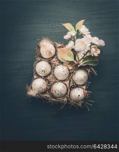 Eggs in carton box with decorative spring blossom on dark gray background, top view. Easter concept
