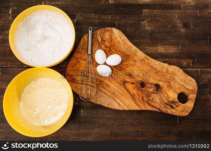 Eggs on wooden cutting board against bowls with cake ingredients top view. Homemade food cooking concept. Dough baking