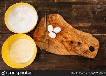 Eggs on wooden cutting board against bowls with cake ingredients top view. Homemade food cooking concept. Dough baking