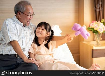 Eight years old girl playing teddy doll with dad in bed in patient ward. Mature asian father encourage her daughter after admission to in patient department in hospital.