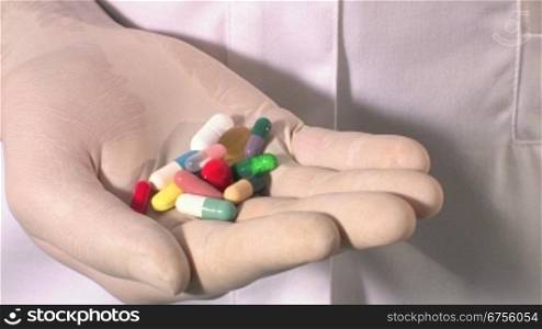 Ein Arzt hSlt mehrere Pillen in der Hand. Er verschliesst die Hand zu einer Faust und ?ffnet diese dann wieder.
