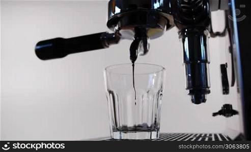 ein Espresso wird wird der Maschine zubereitet und lauft in ein durchsichtiges Glas an espresso machine is started and espresso runs into a transparent cup