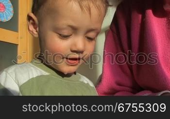 Ein Kind sieht sich mit seiner Mutter ein Bilderbuch an und versucht zu sprechen.Die Mutter erklSrt ihrem Kind was zu sehen ist.