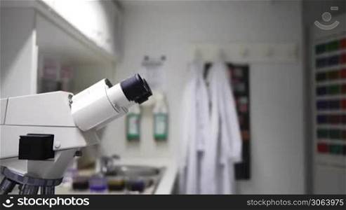 Ein Mann rollt im Laborstuhl vor ein Mikroskop. Male comes and looks in microscope.