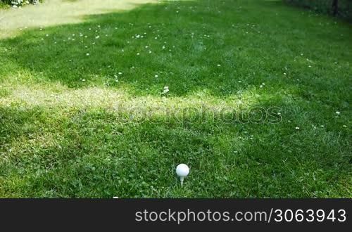 Ein Mann zielt mit dem Golfschlager auf einen Golfball und trifft ihn, der Ball fliegt. A male focuses on a golfball and hits it, the ball is flying.