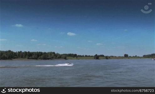 Ein Sportboot fShrt auf dem Rhein bei Tag mit dem Ufer als Hintergrund