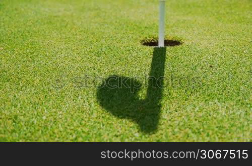 ein starker Schatten bzw. Schlagschatten einer Zielflagge in einem Golfloch ist im wehenden Wind zu sehen - geeignet fur Metaphern wie letzter Schu? ist uberschattet etc.