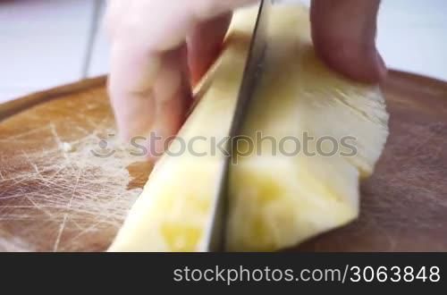 eine Ananas wird vom Koch mit einem scharfen Messer auf einem Holzbrett schnell in kleine Stucke geschnitten, chef cuts a pineapple with a sharp knife quickly in small slices