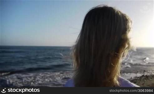 Eine Frau steht am Strand und schaut Richtung Meer. A woman waits on the beach and is looking at the sea.