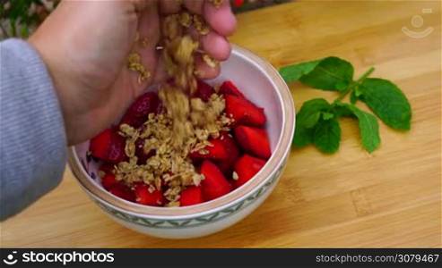 eine Hand streut Musli uber eine Schale geschnittene Erdbeeren zum Fruhstuck